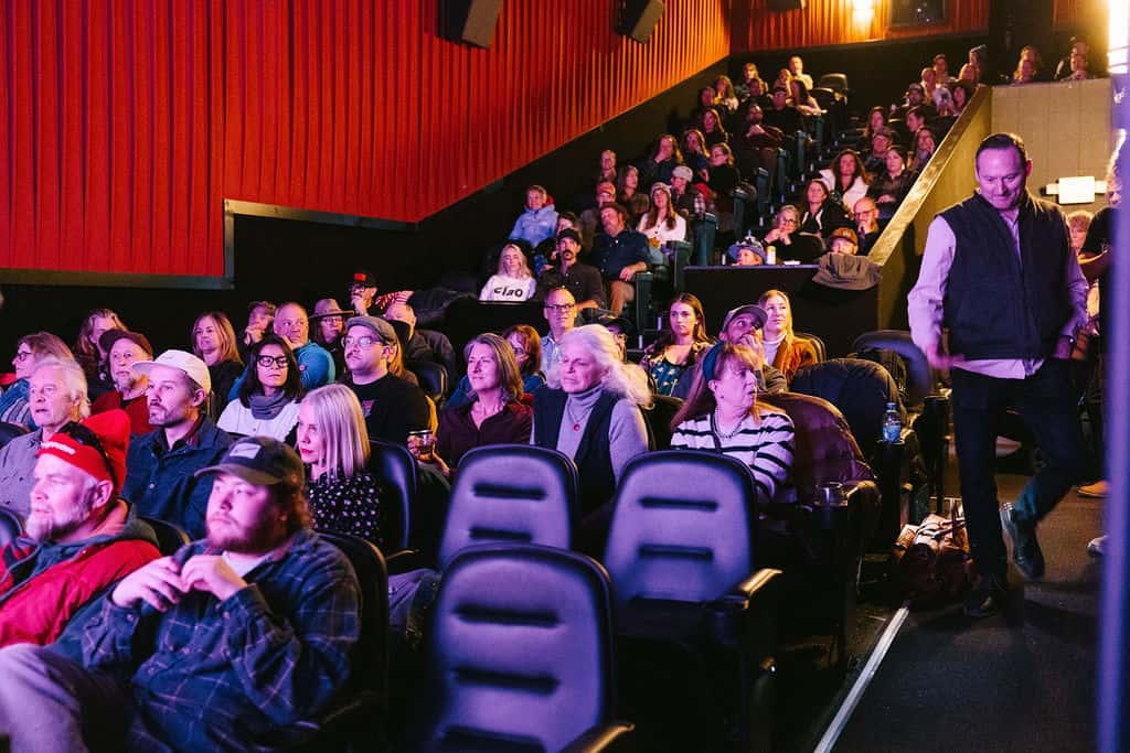 Audience members seated in purple cinema chairs during indoor event presentation.