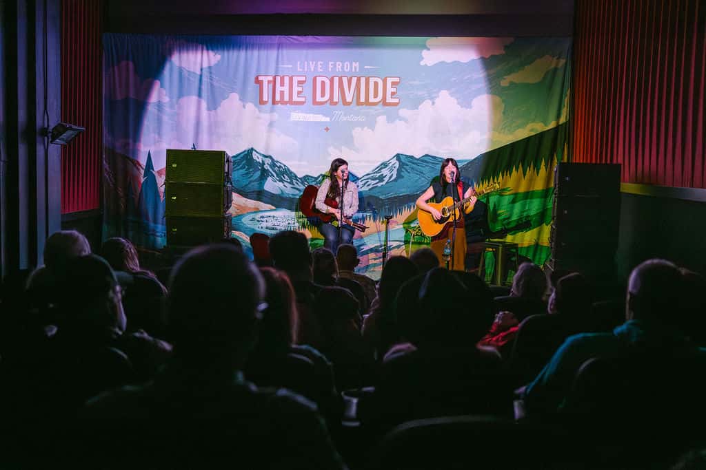 Band performs on stage with "The Divide" backdrop and mountain scenery projection.