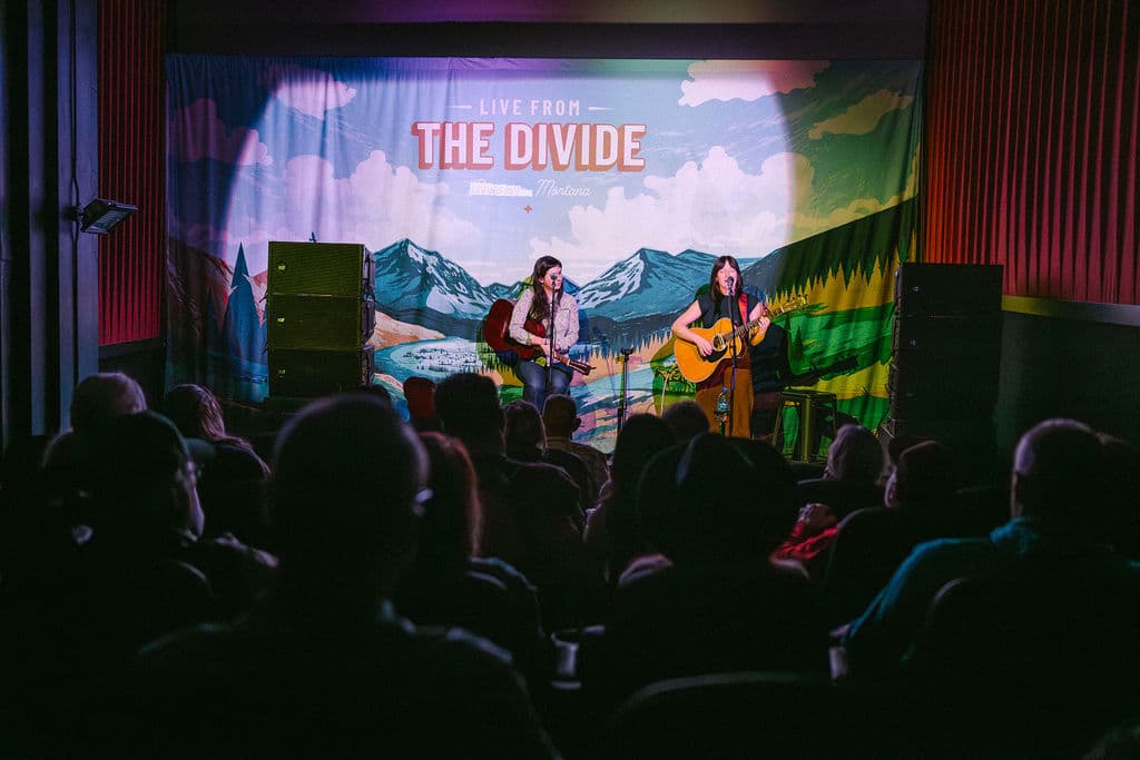 Band performs on stage with "The Divide" backdrop and mountain scenery projection.