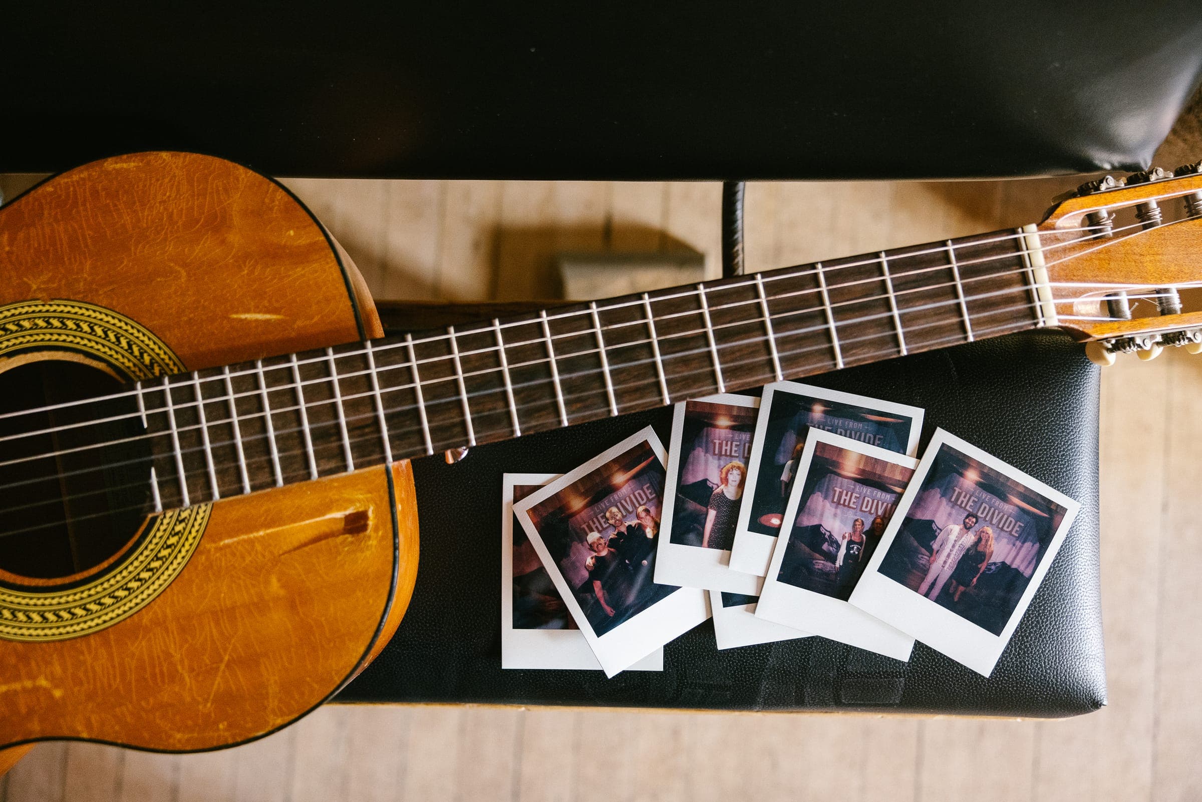 Classical guitar with scattered Polaroid photos on black surface.