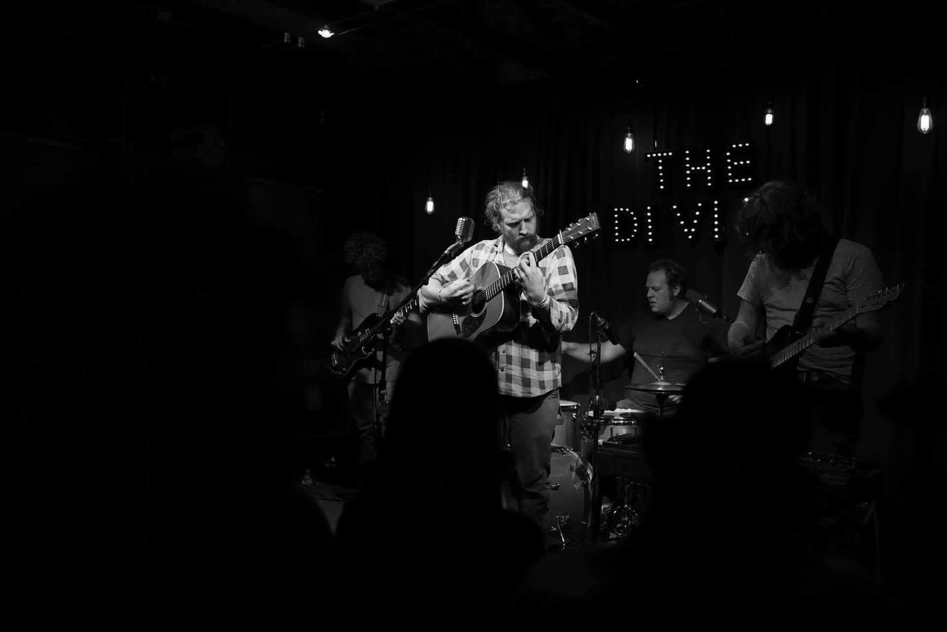 Black and white photo of musician performing with acoustic guitar on stage.