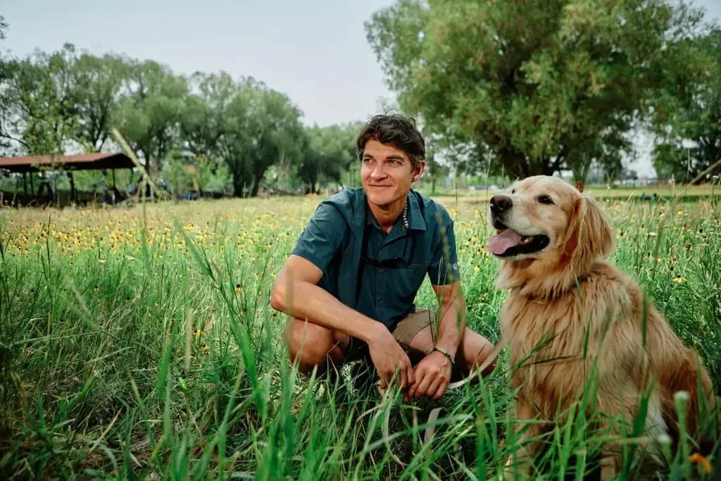 David Weinstein crouching with golden retriever in green field.
